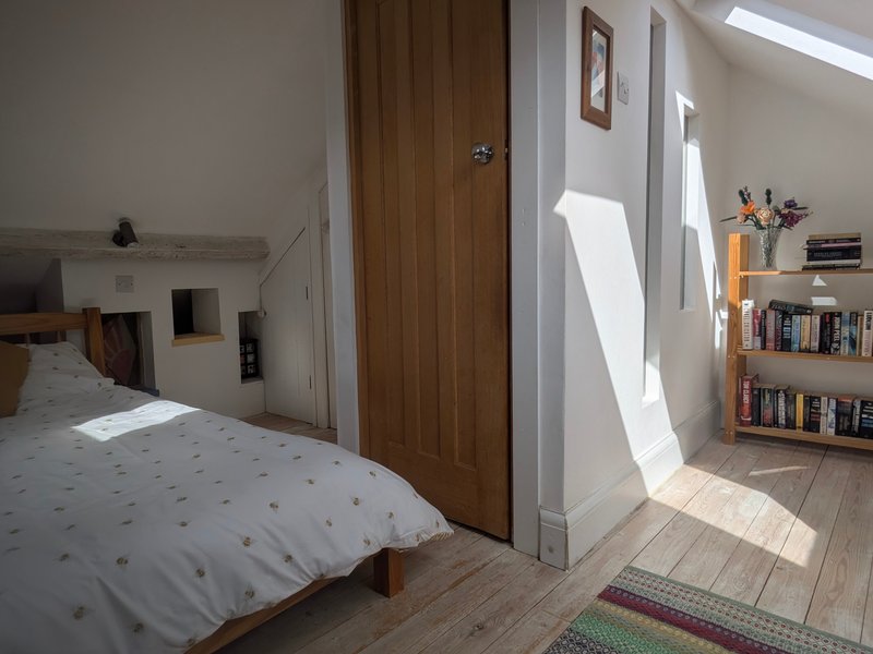 Bright bedroom with single bed, wooden door, bookshelf, and natural light from window