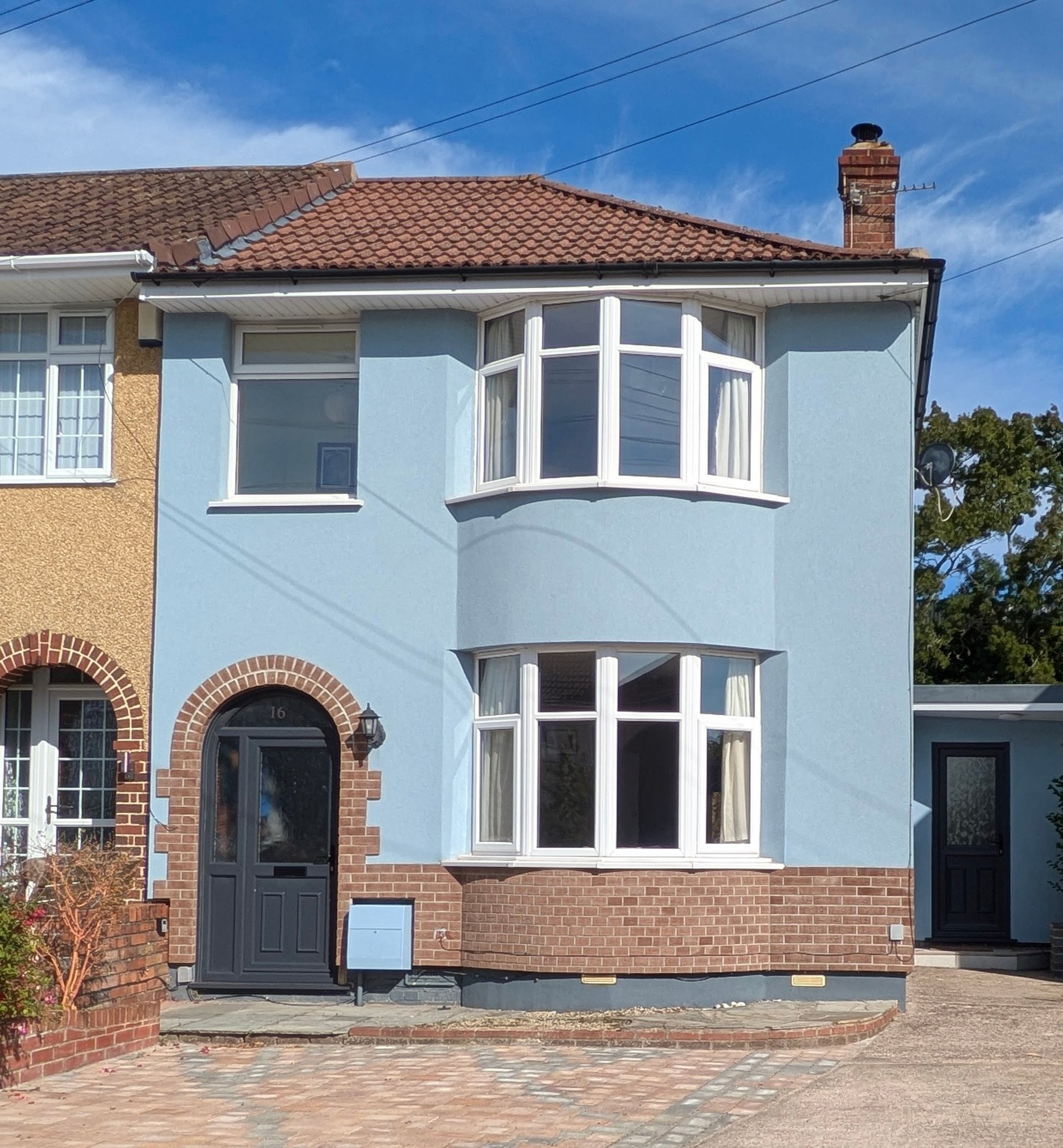 Light blue semi-detached house with brick base, bay windows, tiled roof and brick driveway