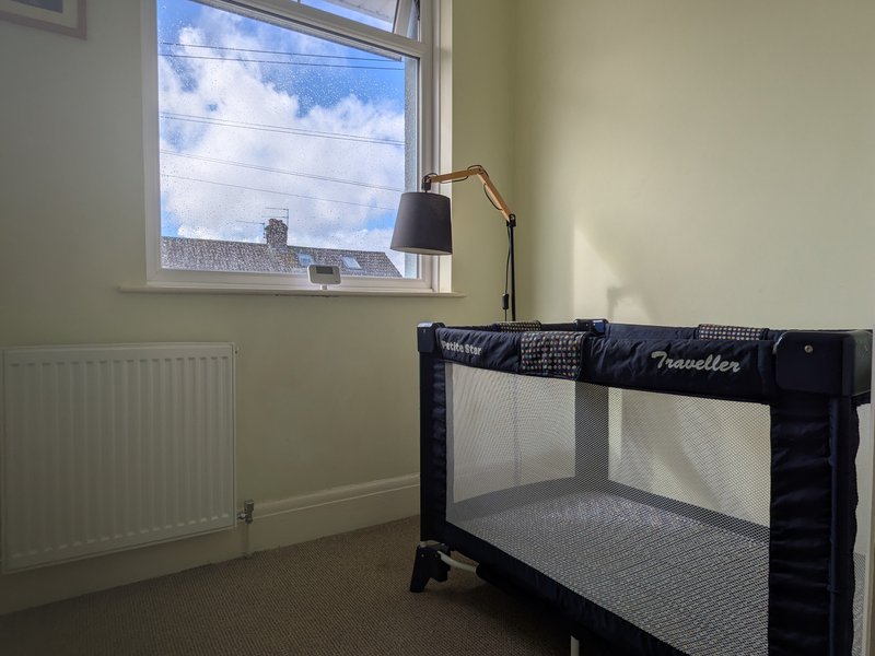 Bedroom with travel cot, desk lamp, radiator and window with city views