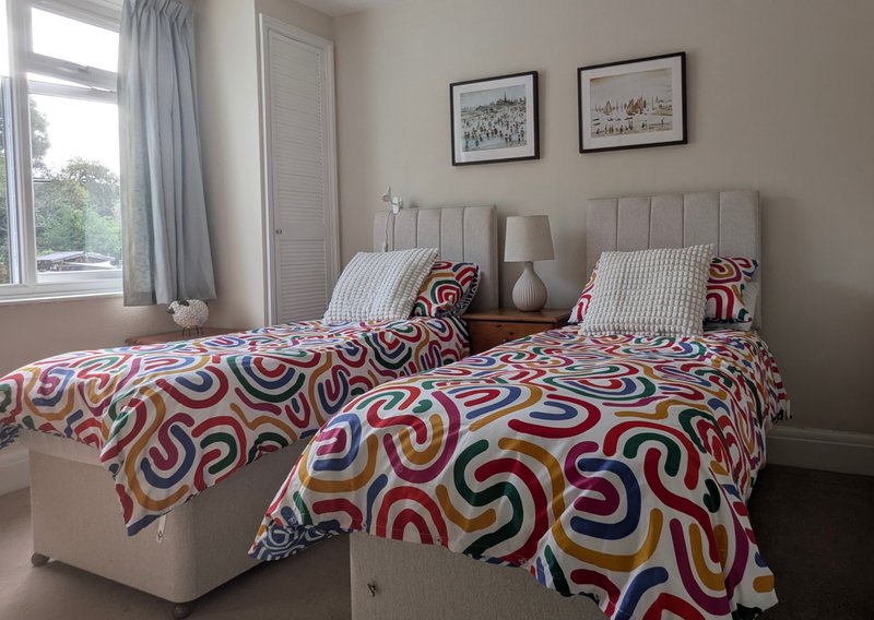Twin bedroom with colourful patterned bedding, upholstered headboards, window with grey curtains