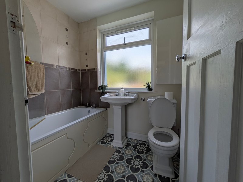 Bathroom with bathtub, pedestal sink, toilet, and window overlooking garden