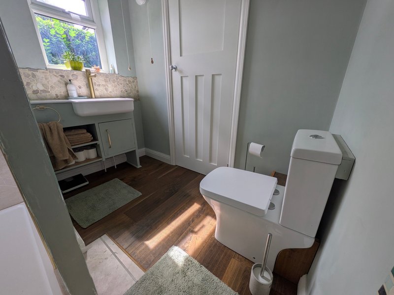 Clean bathroom with toilet, sink vanity, wooden flooring and window with natural light