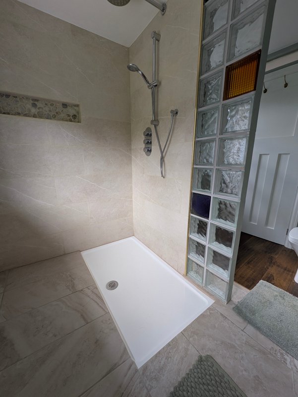 Modern bathroom shower enclosure with white tray, chrome fixtures and glass block partition wall