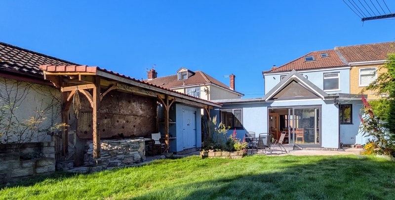 Backyard view of white cottage with wooden pergola, green lawn, and neighboring properties
