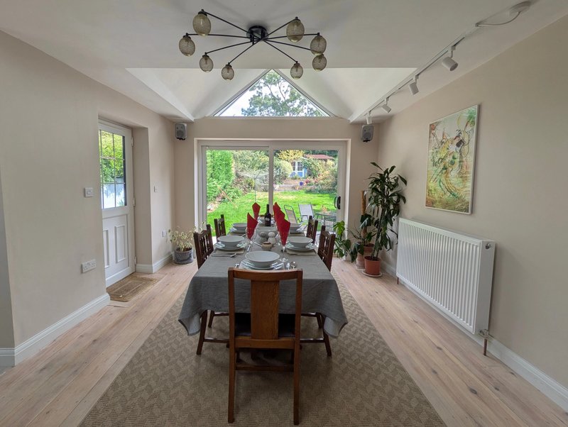 Bright dining room with wooden table, modern chandelier, garden views and potted plants
