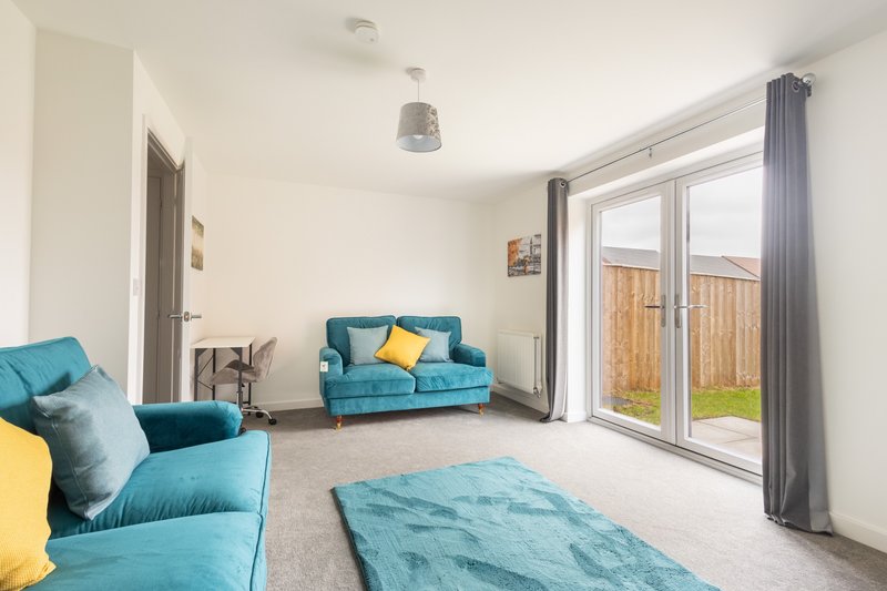 Bright living room with turquoise sofas, yellow cushions, gray carpet and glass doors to garden