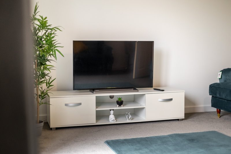 Modern living room with white TV unit, flat-screen television, potted plant and teal armchair