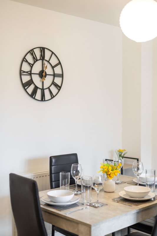 Dining table set for two with wall-mounted decorative clock and round ceiling light
