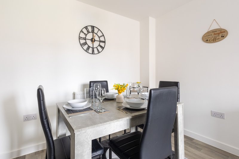 Dining area with gray table, black chairs, wall clock, and place settings