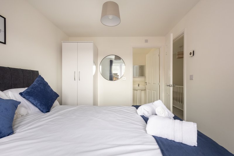 Modern bedroom with double bed, blue cushions, white wardrobe and circular mirror