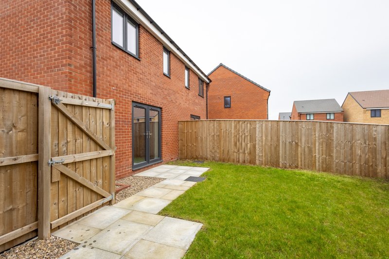 Brick house exterior with wooden fence, patio, green lawn and garden gate