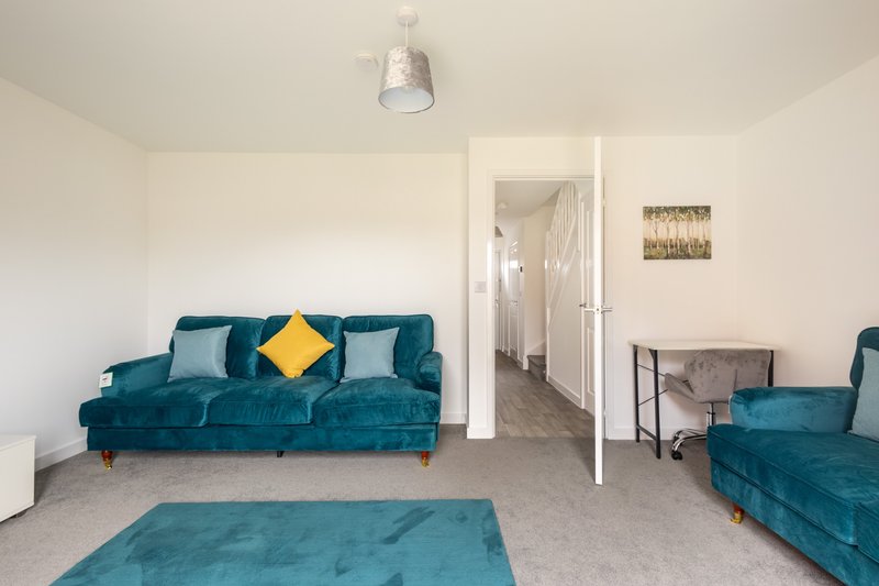 Living room with two teal velvet sofas, yellow cushion, gray carpet, and white ceiling light
