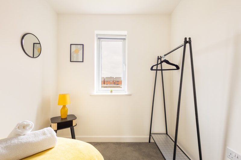 Minimalist bedroom with yellow lamp, white pillows, clothing rack and circular wall art
