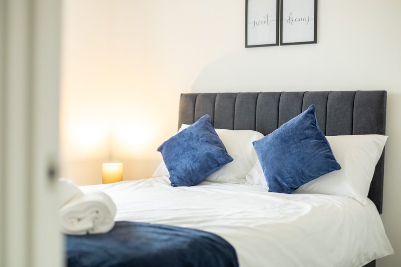 Modern bedroom with gray upholstered headboard, white bedding, and blue decorative pillows