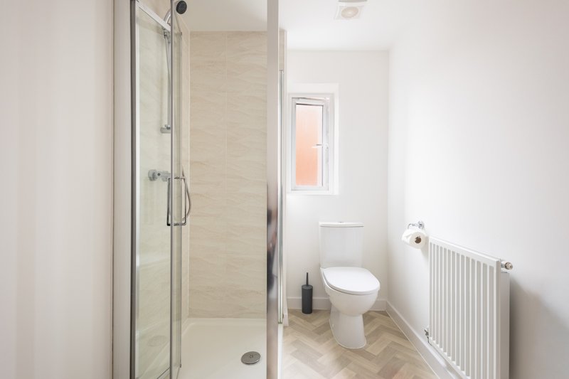 Clean modern bathroom with shower enclosure, toilet, radiator and small window
