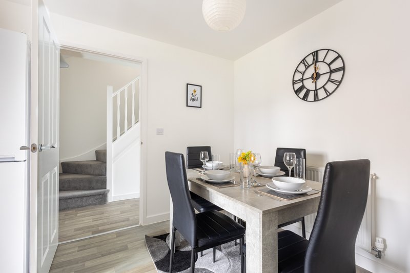 Modern dining area with wooden table, black chairs, wall clock and staircase entrance