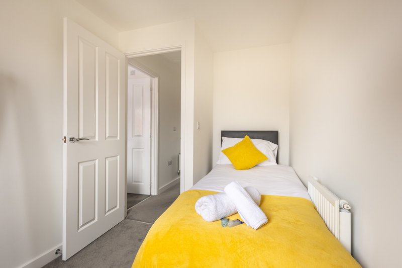 Bright bedroom with single bed, yellow bedding, white pillows and rolled towels