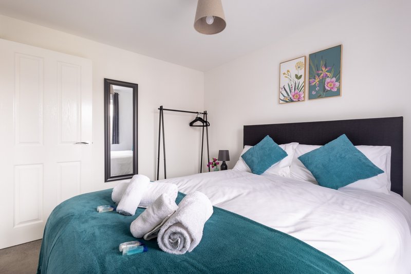 Modern bedroom with double bed, teal pillows, white bedding, and framed wall art