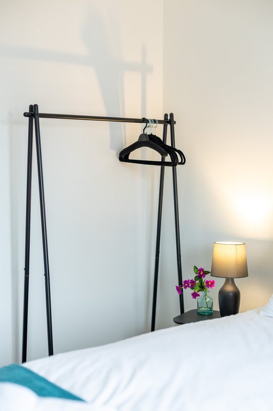 Bedroom corner with clothing rail, black hanger, bedside lamp and small potted flowers