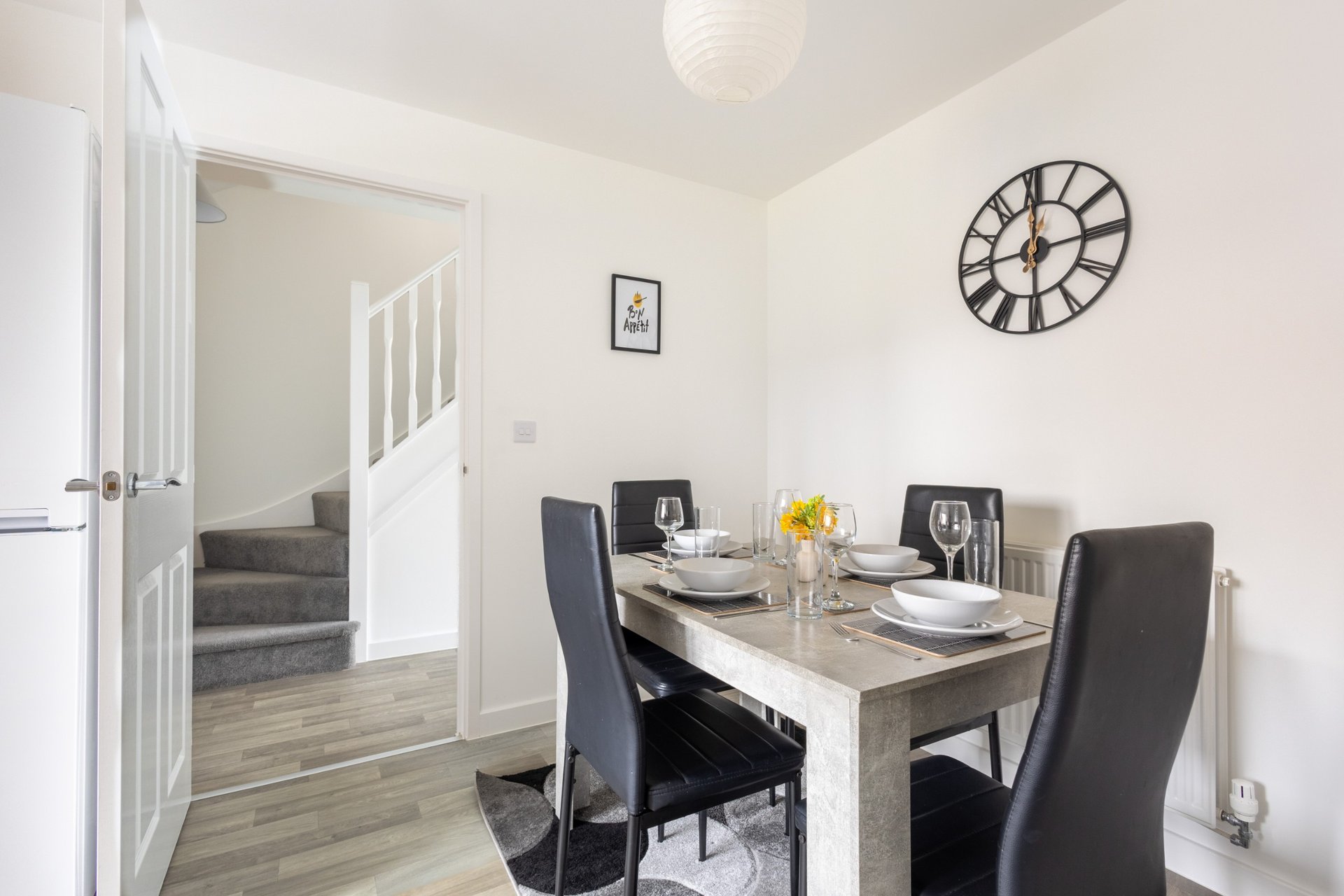 Dining area with wooden table, black chairs, wall clock, and doorway to hallway