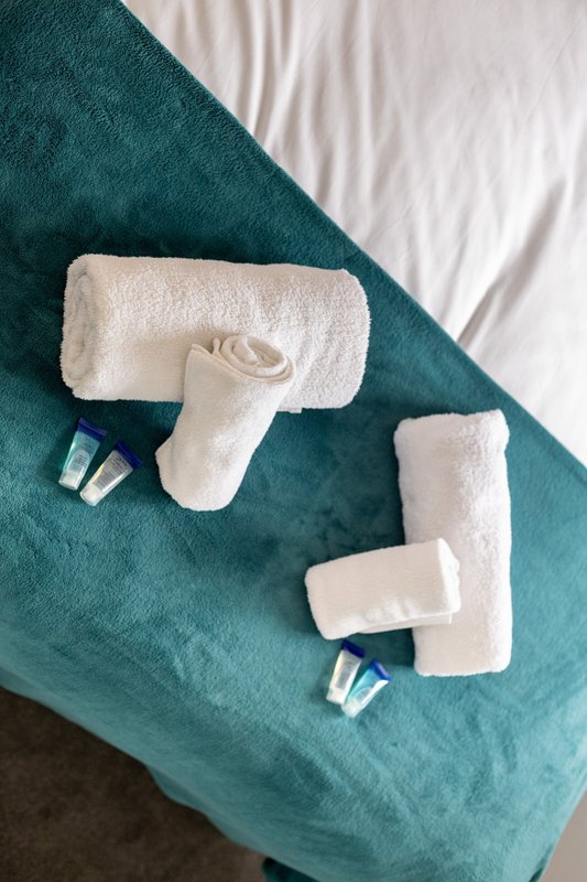 Rolled white towels and toiletries arranged on teal and white bedding