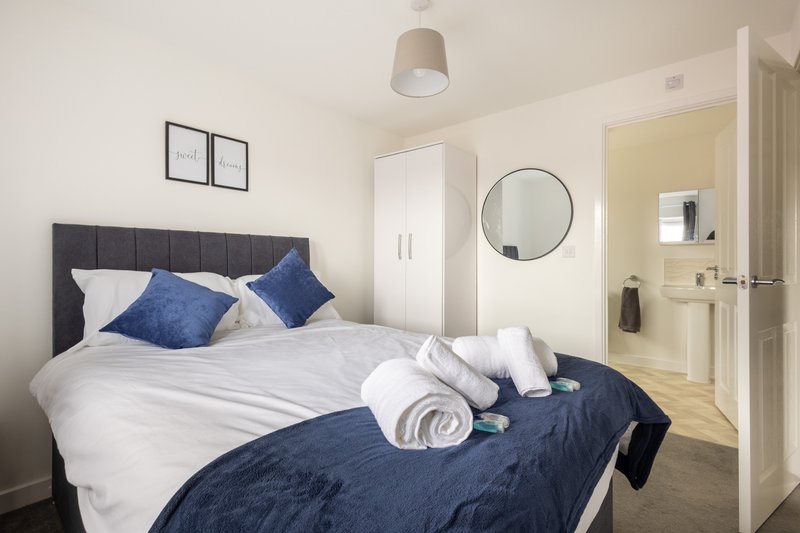 Modern bedroom with double bed, blue and white bedding, dark headboard, and en-suite bathroom door visible