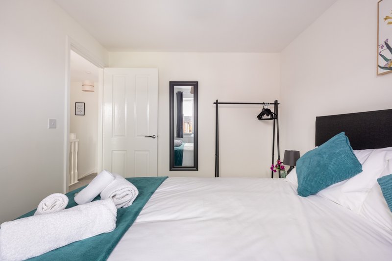 Modern bedroom with double bed, teal cushions, black headboard and industrial lamp