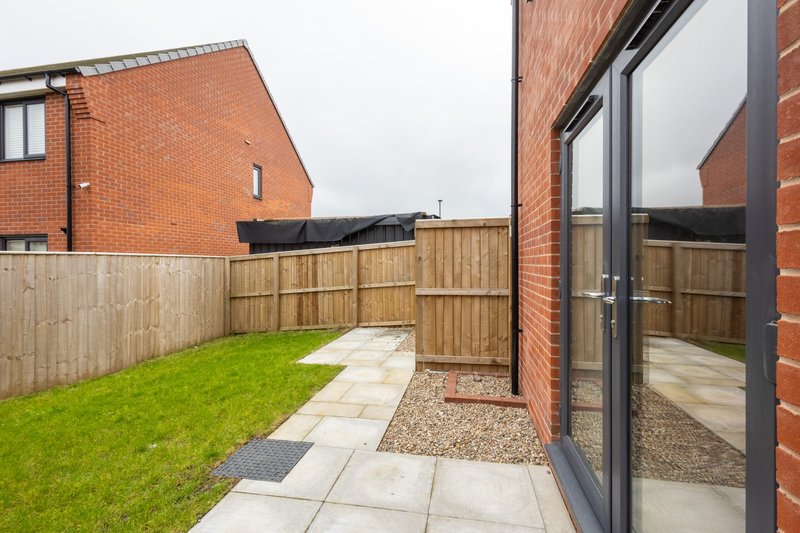 Modern brick house with garden patio, lawn, wooden fence and paved pathway