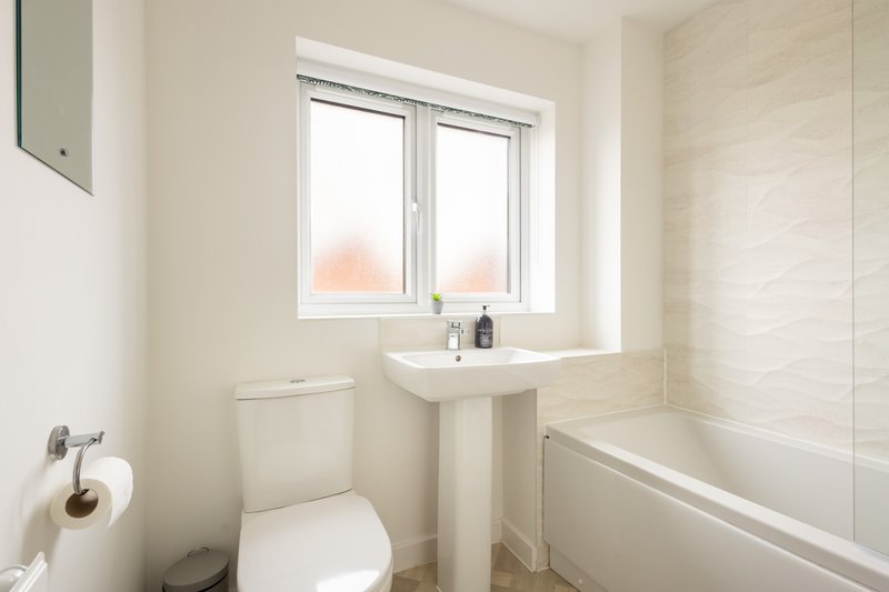Clean modern bathroom with toilet, pedestal sink, bathtub and window