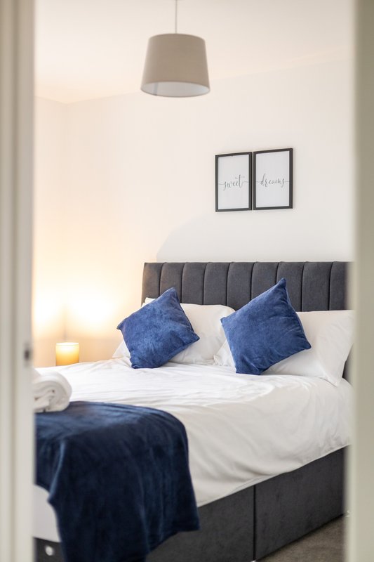 Modern bedroom with grey upholstered bed, white bedding, blue cushions and pendant lamp