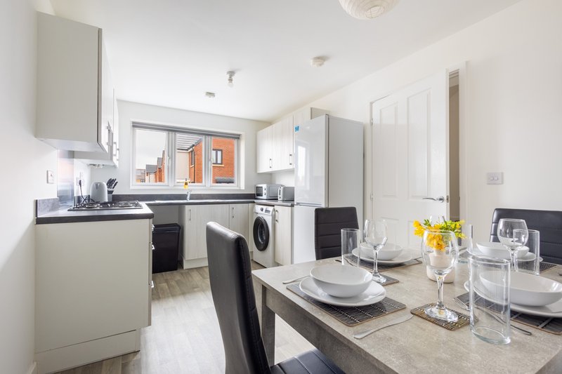 Modern kitchen-diner with white appliances, dining table set for four, and view to garden