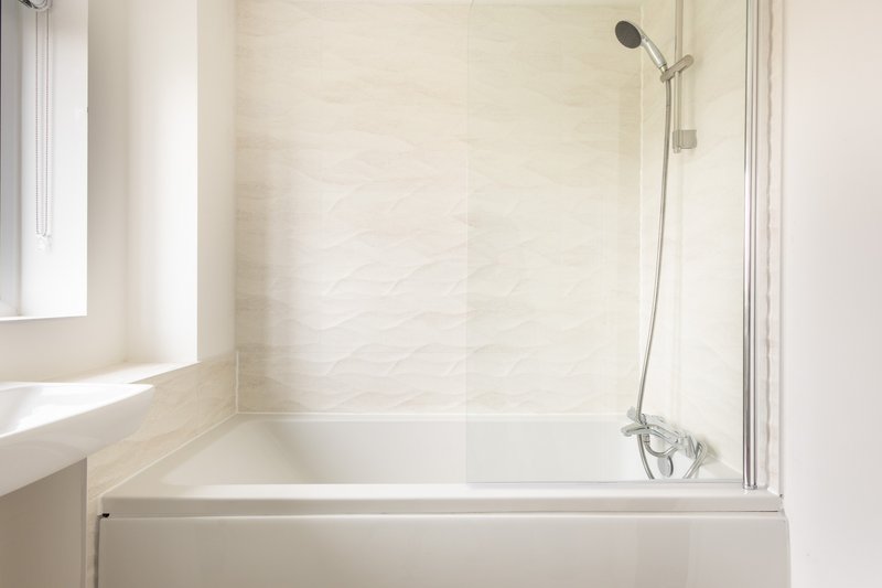 Clean modern bathroom with white tile walls, bathtub and shower enclosure