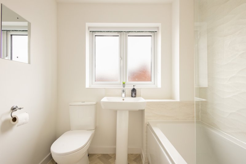Modern bathroom with toilet, pedestal sink, bathtub and frosted window