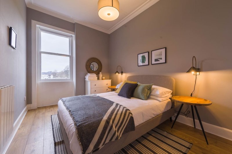 Modern bedroom with double bed, wooden floor, bedside lamp and window view