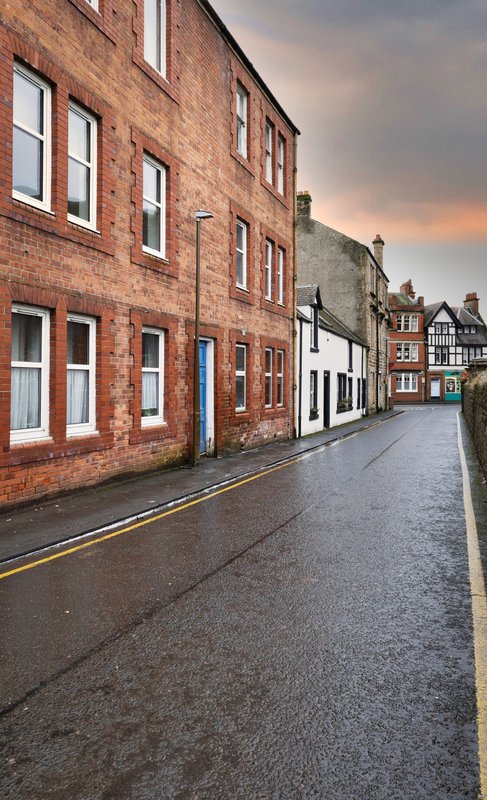 Historic brick street with period buildings, wet pavement, and evening sky