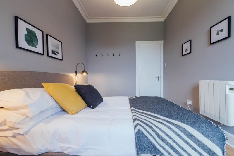Modern bedroom with double bed, yellow and navy cushions, framed wall art, white door and radiator