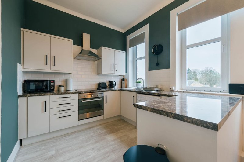 Modern kitchen with white cabinetry, dark granite countertop, stainless steel appliances and teal accent wall