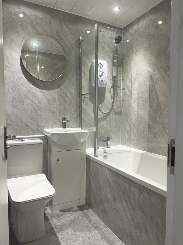 Modern bathroom with grey marble tiles, glass shower enclosure, white basin and toilet