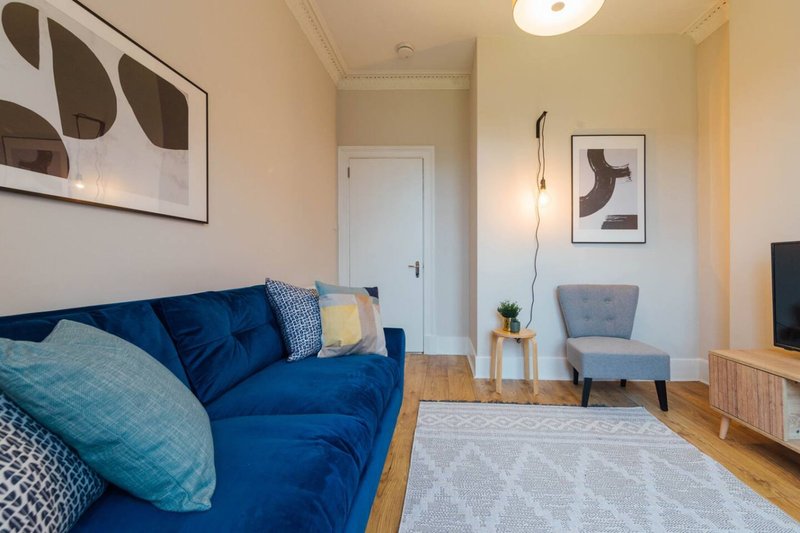 Modern living room with blue sofa, gray armchair, wooden floor and wall art