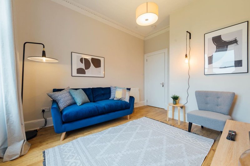 Modern living room with blue sofa, gray armchair, wooden floor and framed wall art