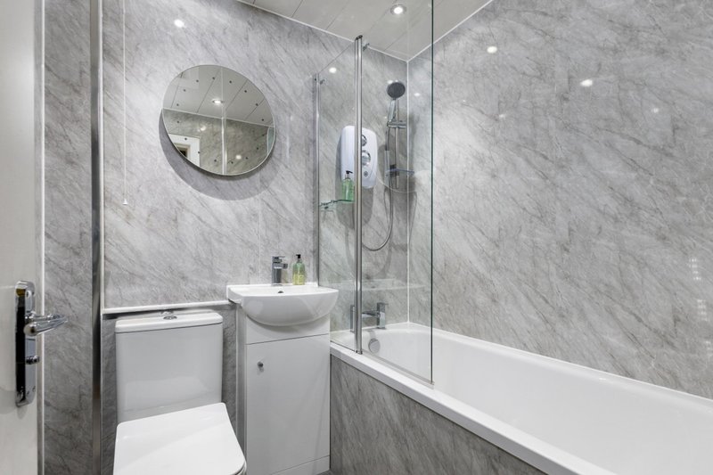 Modern bathroom with grey marble tiles, white sink vanity, toilet, and glass shower enclosure
