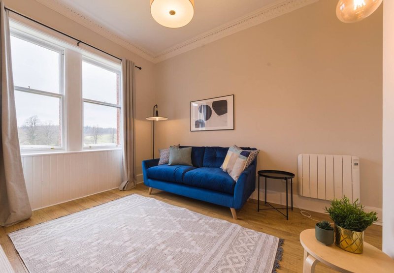 Bright living room with blue sofa, large windows, wooden flooring and neutral décor
