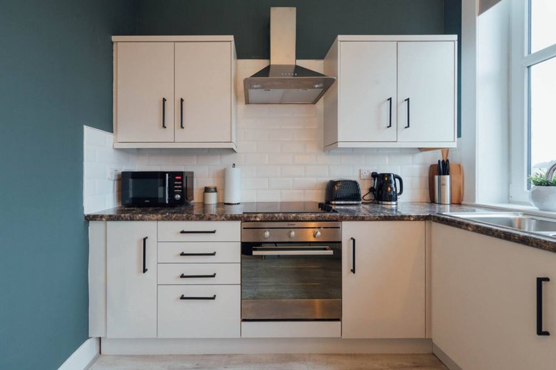 Modern kitchen with white cabinetry, stainless steel appliances, teal accent wall and window