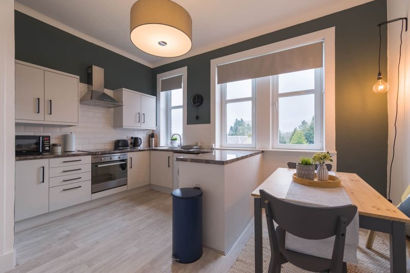 Modern kitchen with white cabinetry, dark feature wall, island with seating, and dining table
