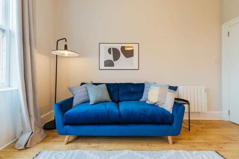 Modern living room with bright blue sofa, floor lamp, wooden floors and abstract wall art