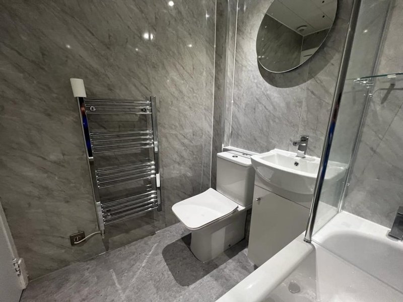 Modern bathroom with gray tile walls, white toilet, sink, heated towel rail, and shower enclosure