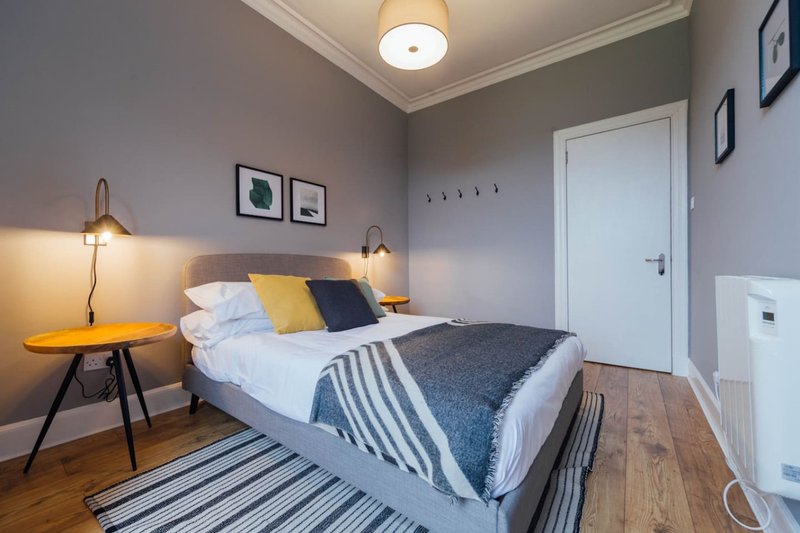 Modern bedroom with double bed, yellow and blue pillows, wooden floor and pendant lamps
