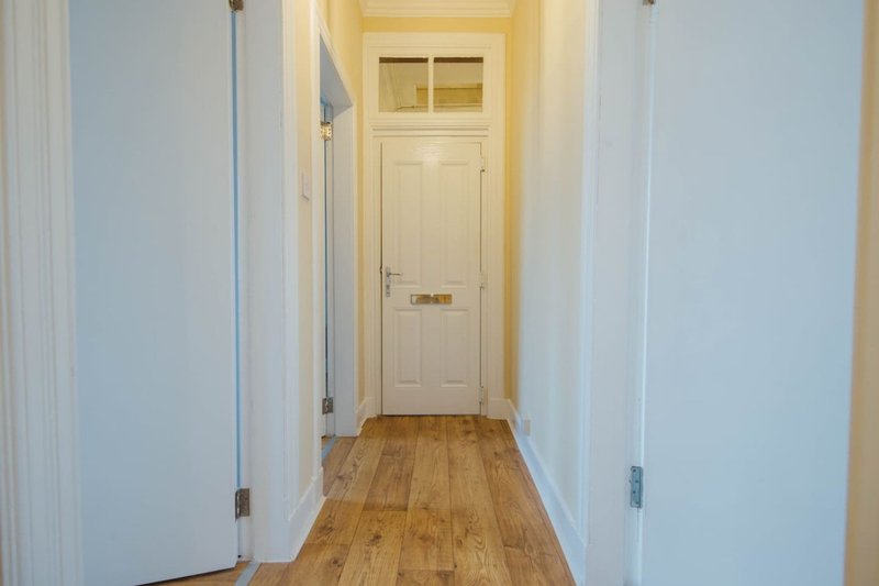 Bright hallway with wooden floor, white doors, and cream-colored entrance door at end