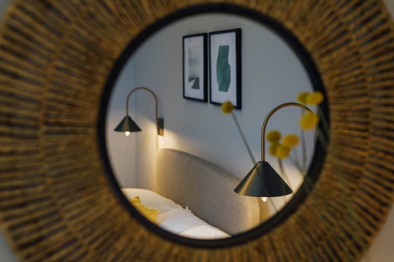 Bedroom viewed through circular mirror, showing bed, arc lamps, and wall art
