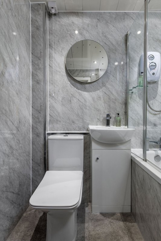 Modern bathroom with marble tiles, round mirror, white toilet and sink vanity